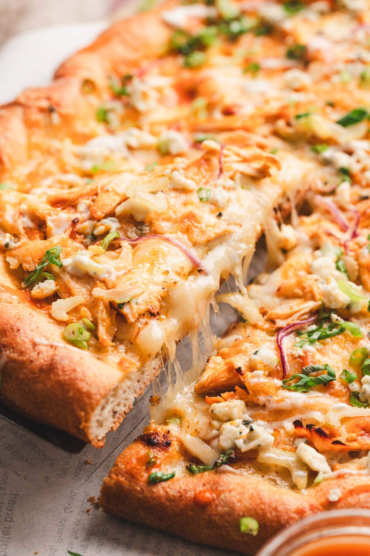 Slice of Buffalo Chicken Pizza with garnish of green onions and blue cheese.