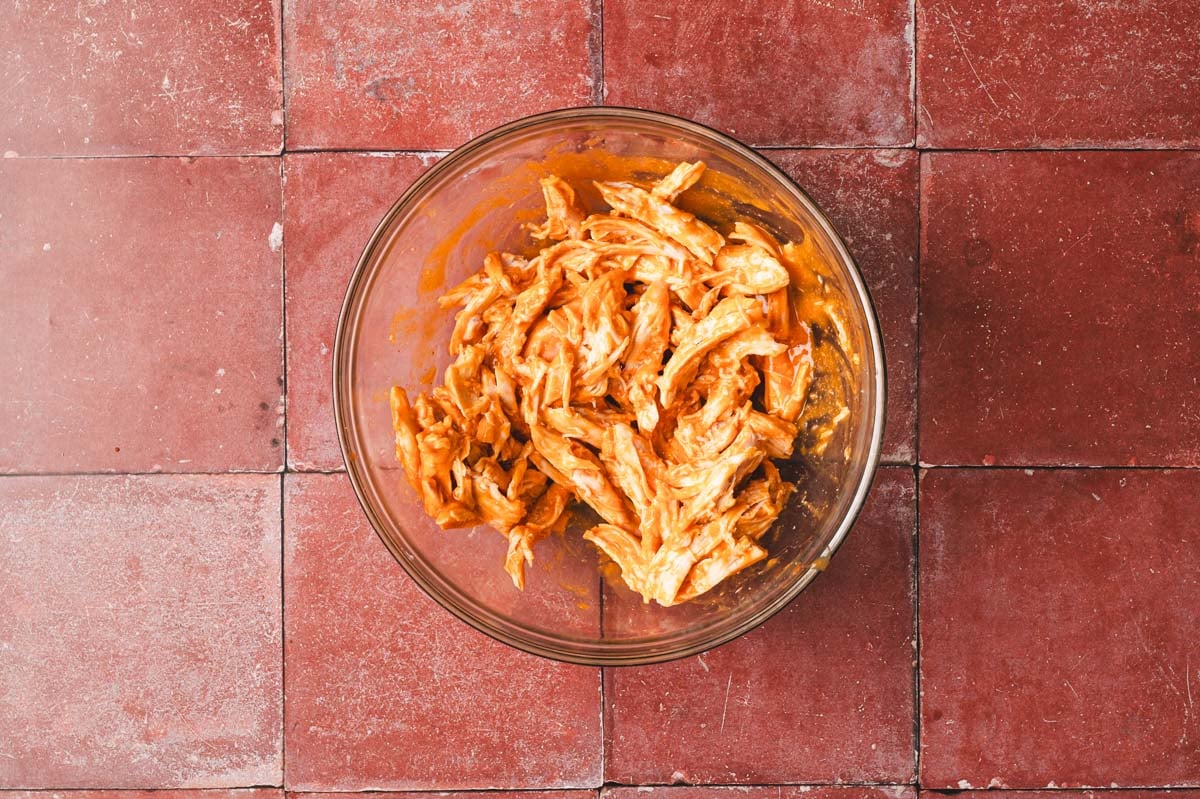 Chicken with buffalo sauce in a glass bowl.