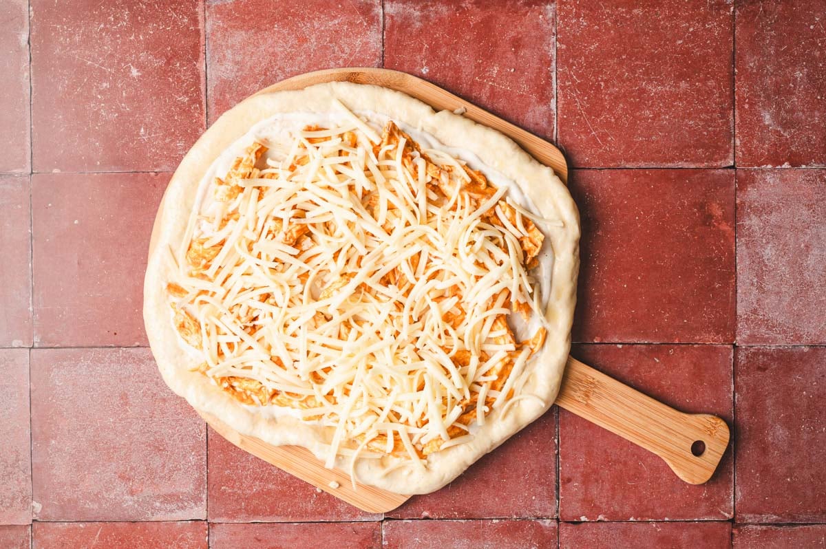 Unbaked pizza with ranch, buffalo chicken, and cheese on top.