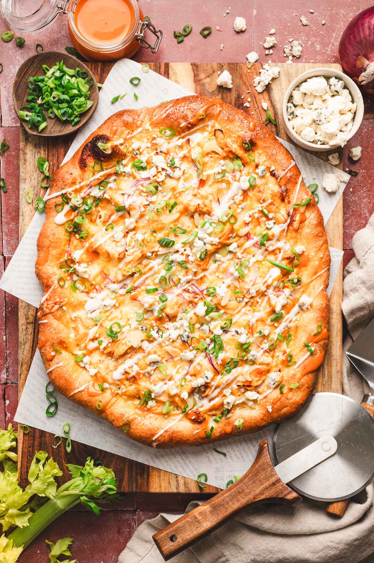 Buffalo Chicken Pizza on a wooden cutting board with a pizza cutter.