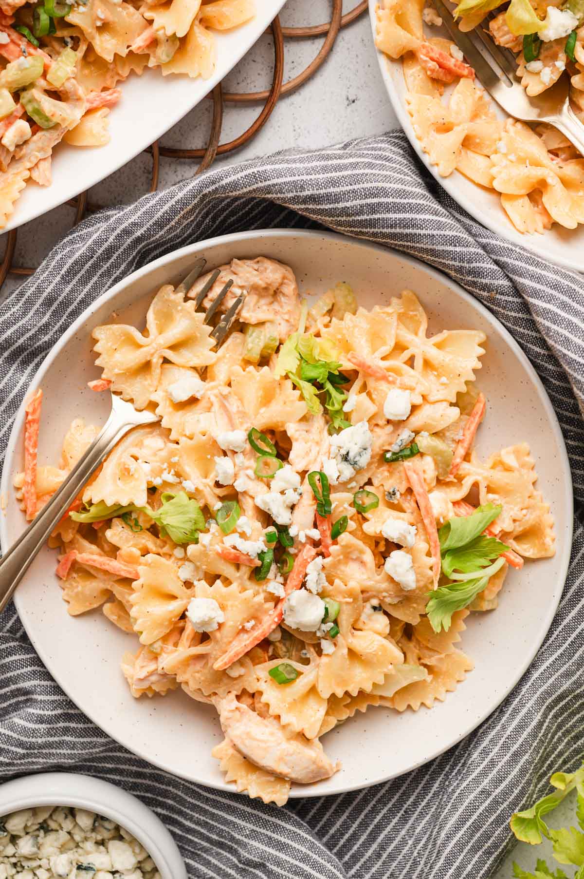 A plate of buffalo chicken pasta salad with a fork and green onion garnish.