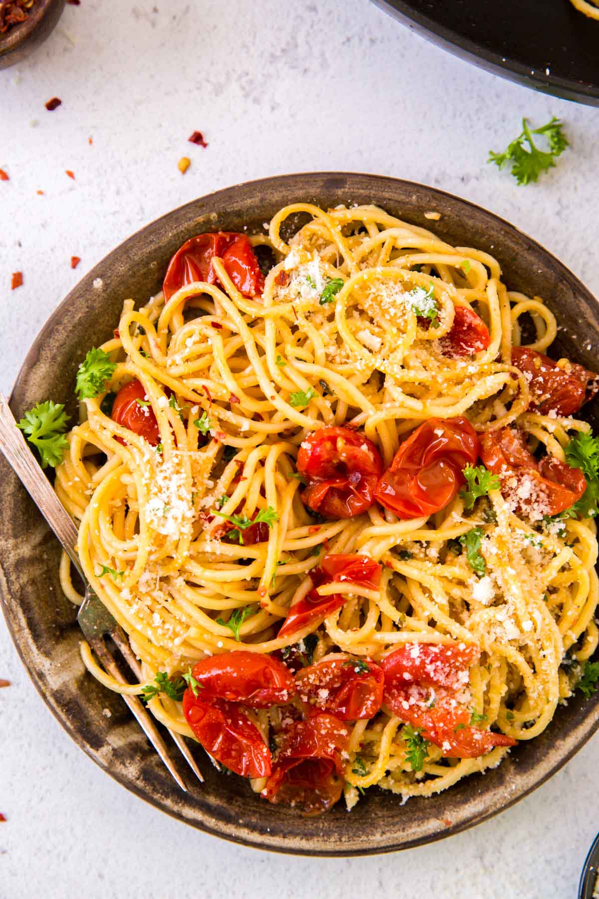 Garlic tomato pasta with parmesan and parsley on top in a large stone bowl.