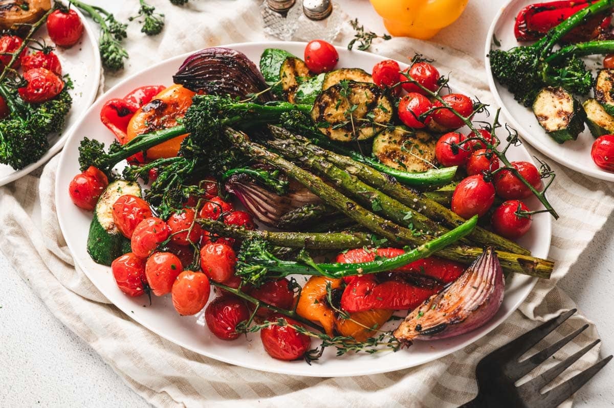 Platter full of grilled vegetables including asparagus, broccolini, tomato, zucchini, onion, and peppers.