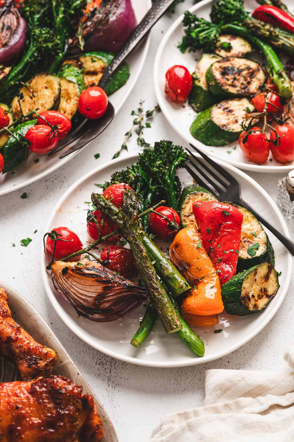 Grilled Vegetables including broccolini, zucchini, tomatoes, and onion on white plates with black forks. 