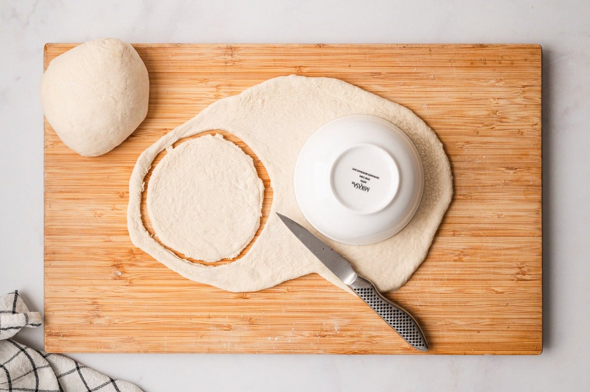 Pizza dough for mini calzones on a cutting board after being cut into circles.