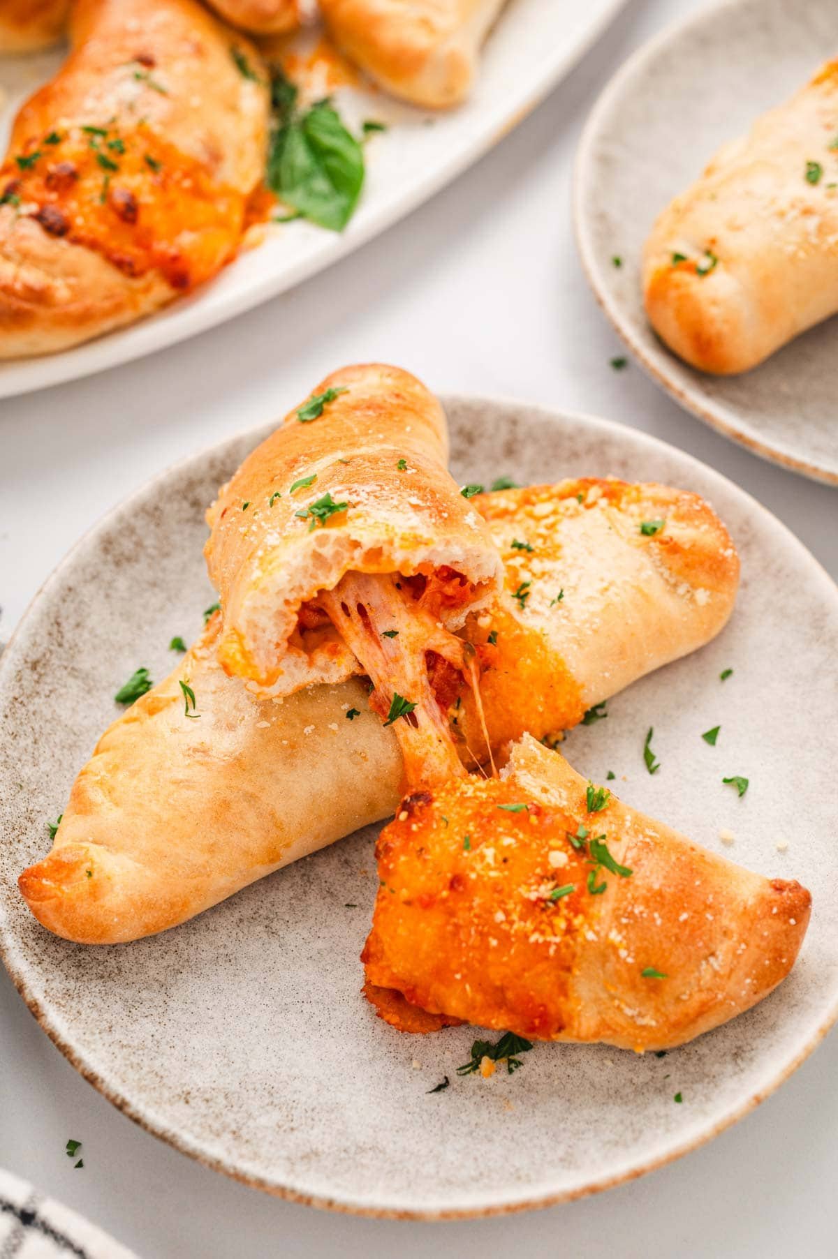 Cooked mini calzones on a plate with one split in half and cheese stretching between the halves.