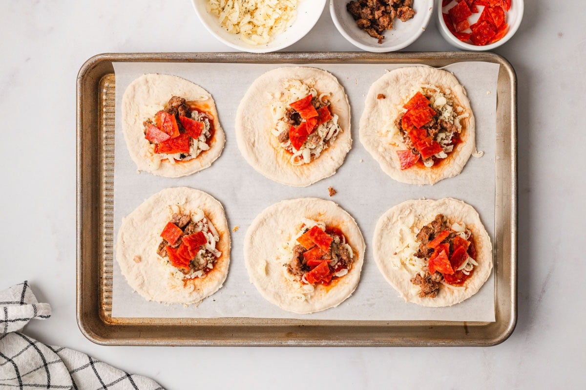 Rounds of pizza dough places on a parchment-lined baking sheet and topped.