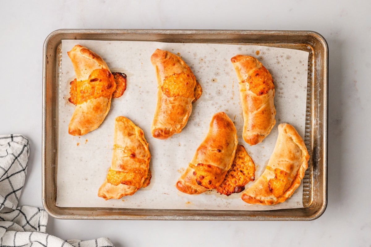 Mini Calzones after being baked in the oven that are golden brown and a few have cheese melting out.