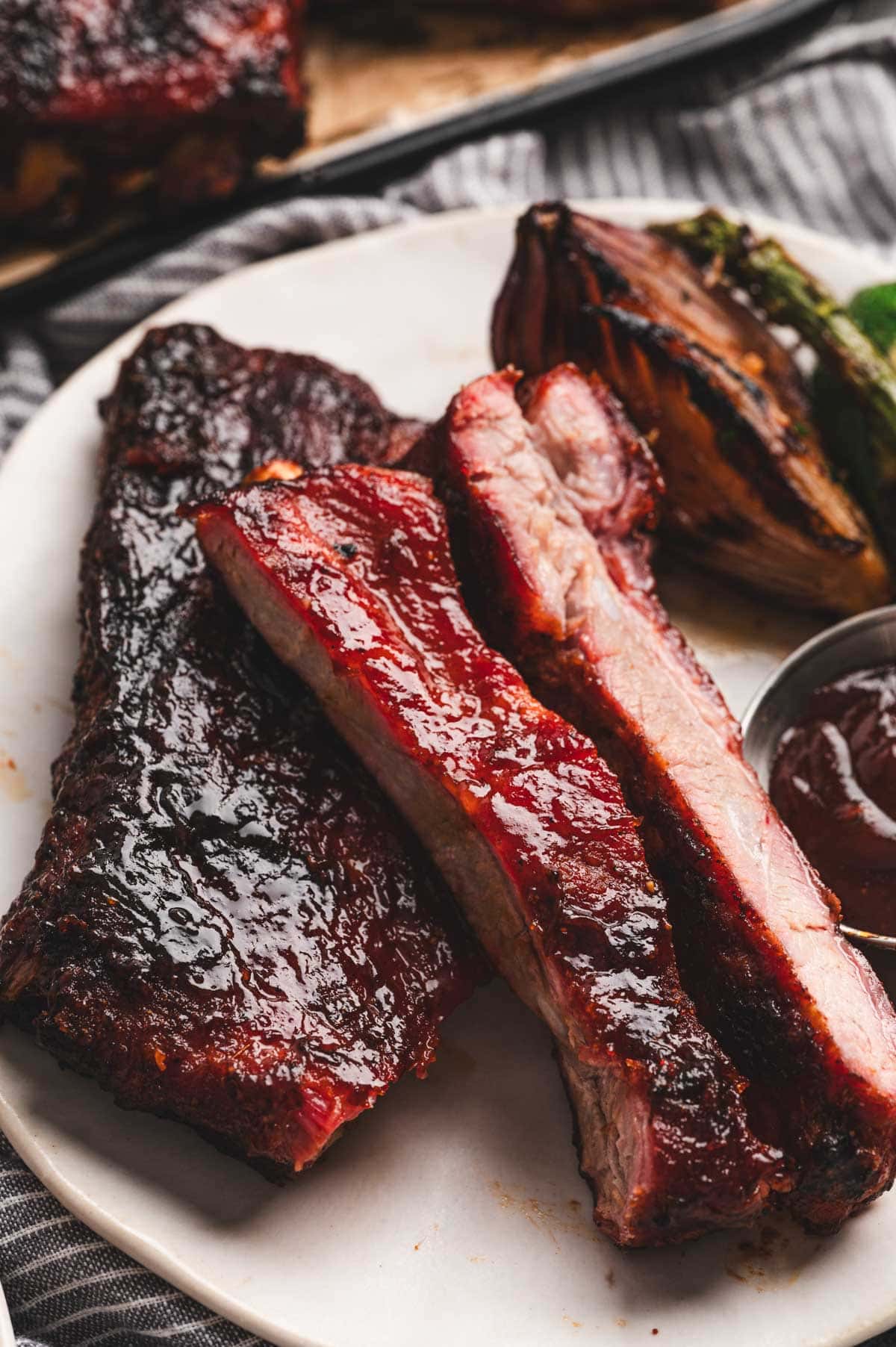 Sliced St. Louis Ribs on a white platter with BBQ Sauce on top.