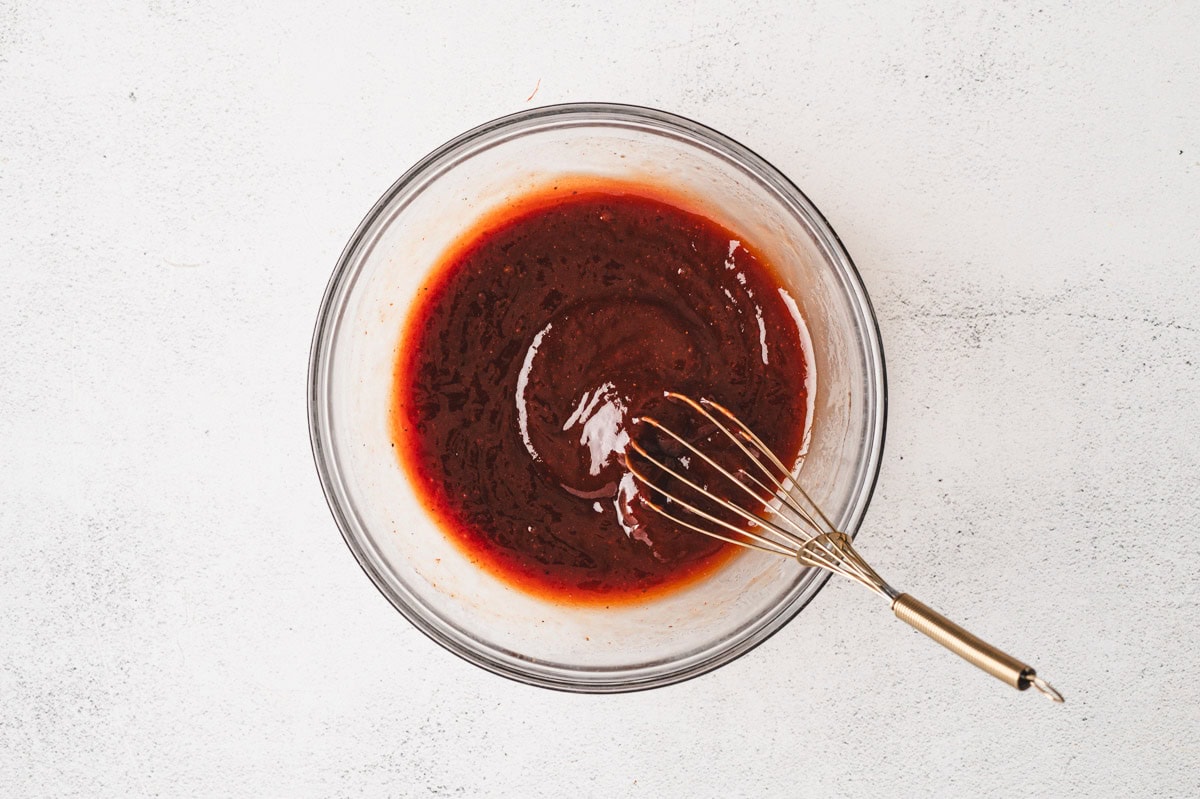 Homemade BBQ sauce in a glass bowl with a whisk.