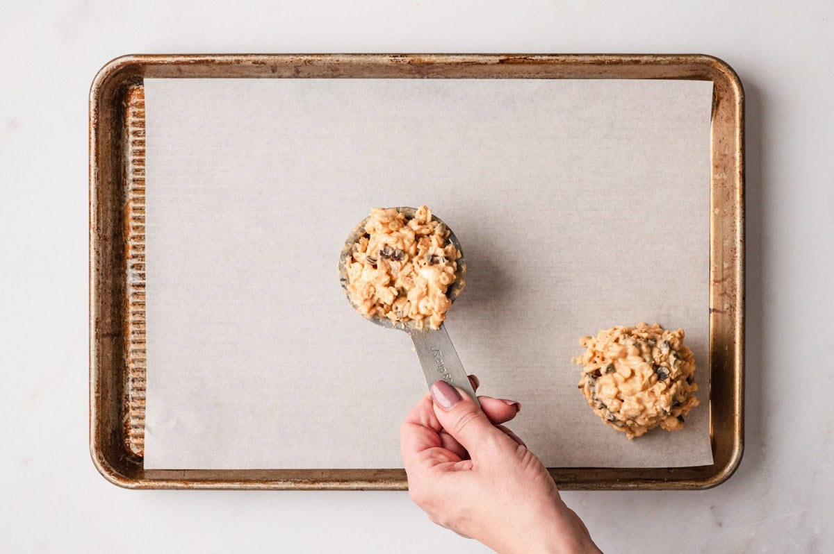 Scoops of the avalanche cookie mix being placed onto a parchment-lined baking sheet.