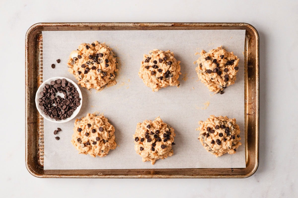 Avalanche cookie mix after being portioned onto a parchment-lined baking sheet with mini chocolate chips on top.