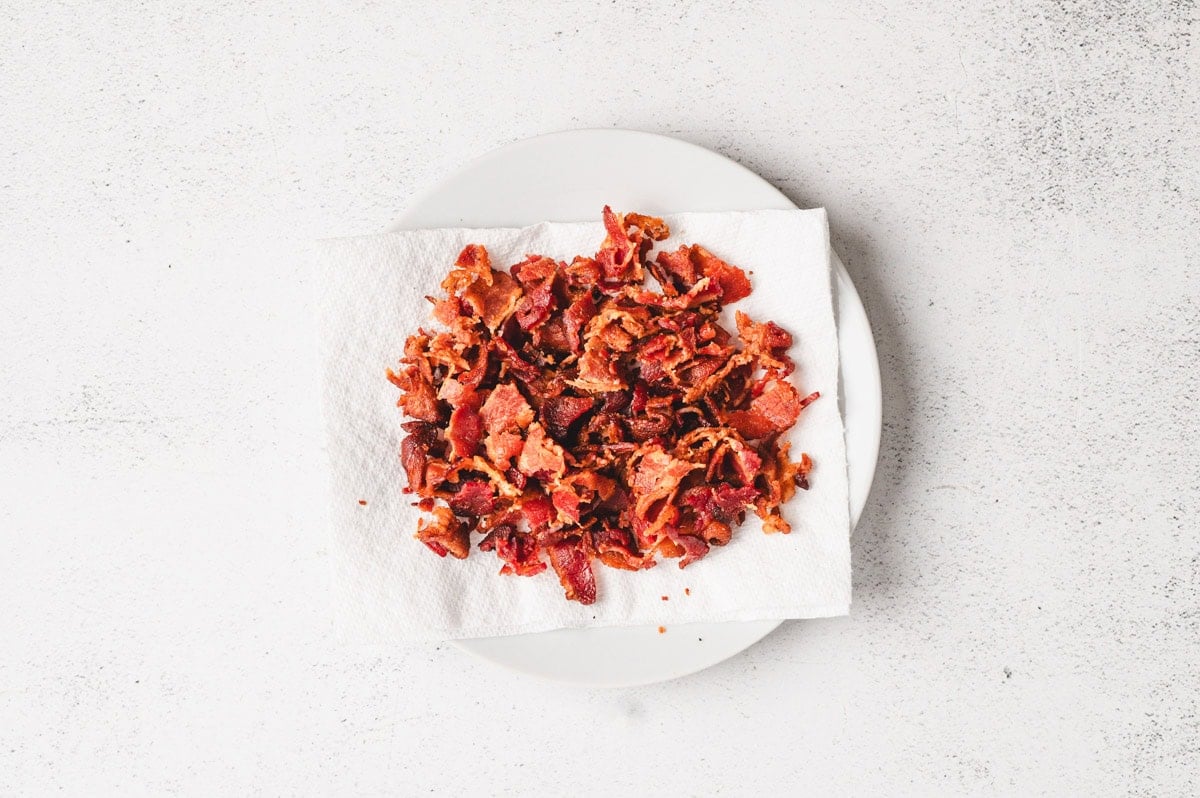 Crispy bacon pieces on a paper towel on a white plate.