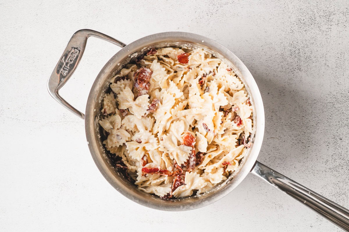 Creamy bowtie pasta with bacon in a stainless steel pan.