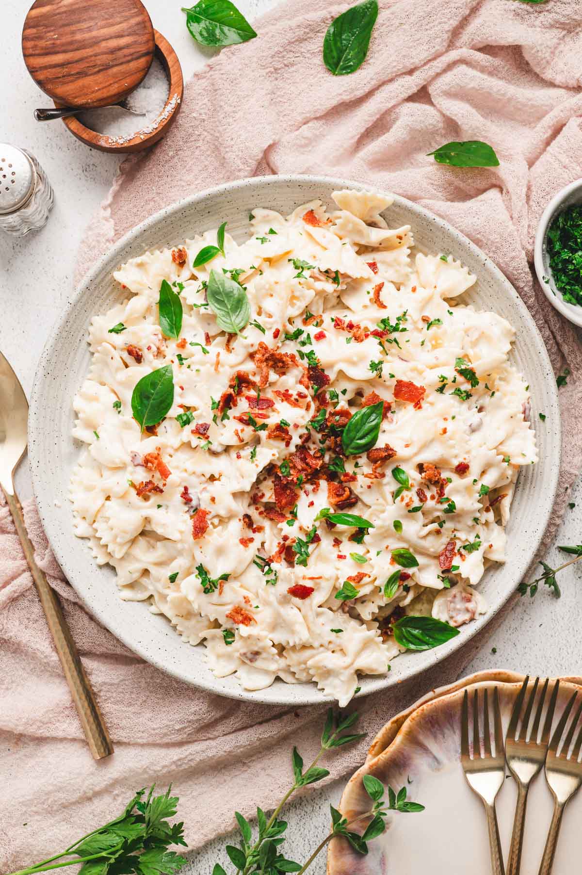 Bowtie pasta with a creamy sauce, bacon and herbs on a white ceramic plate.