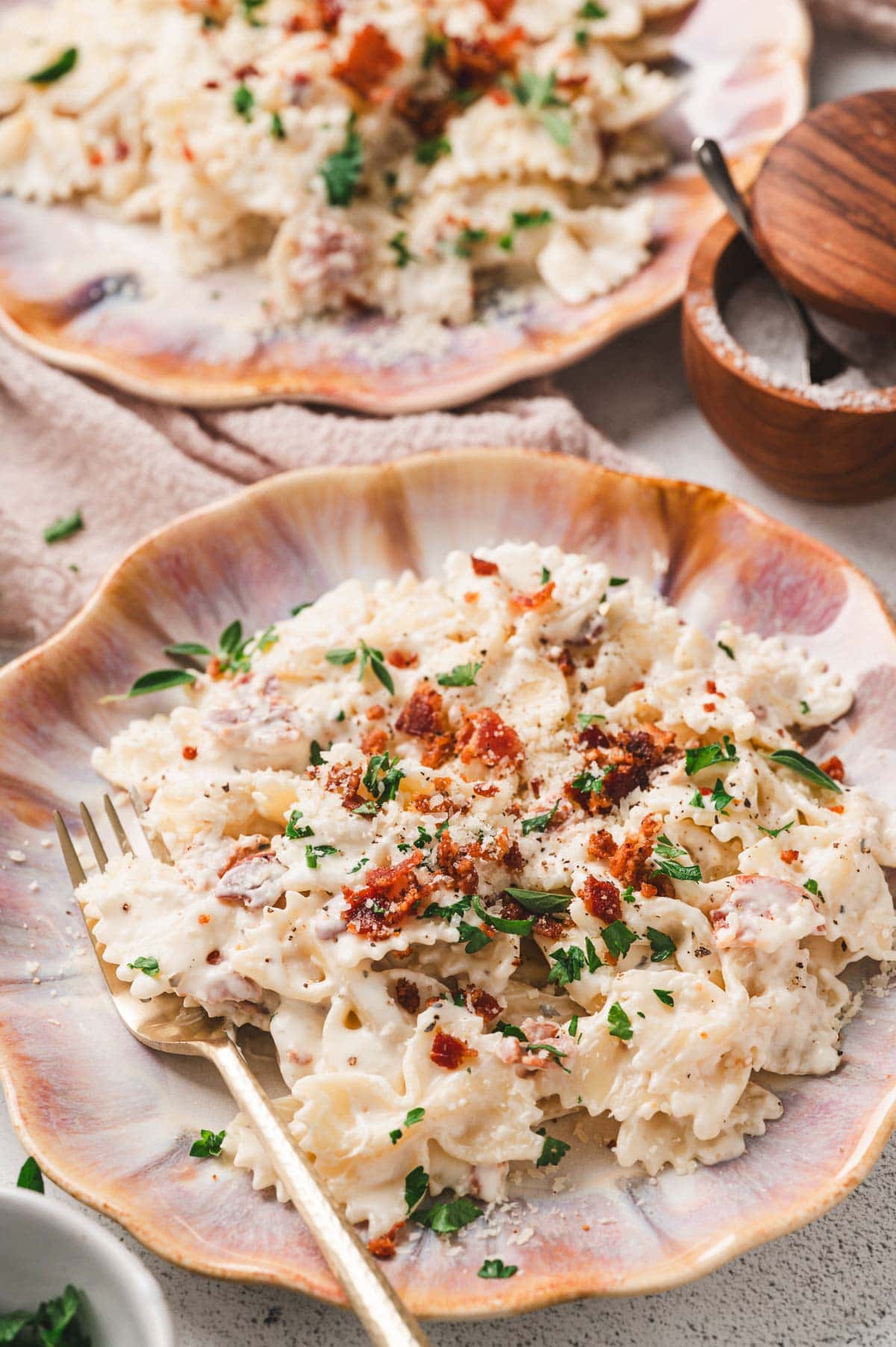 Bowtie pasta with a cream sauce, bacon, and herbs on a decorative plate with a fork.