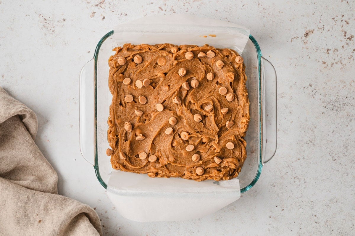 Uncooked blondie dough in a glass baking dish.