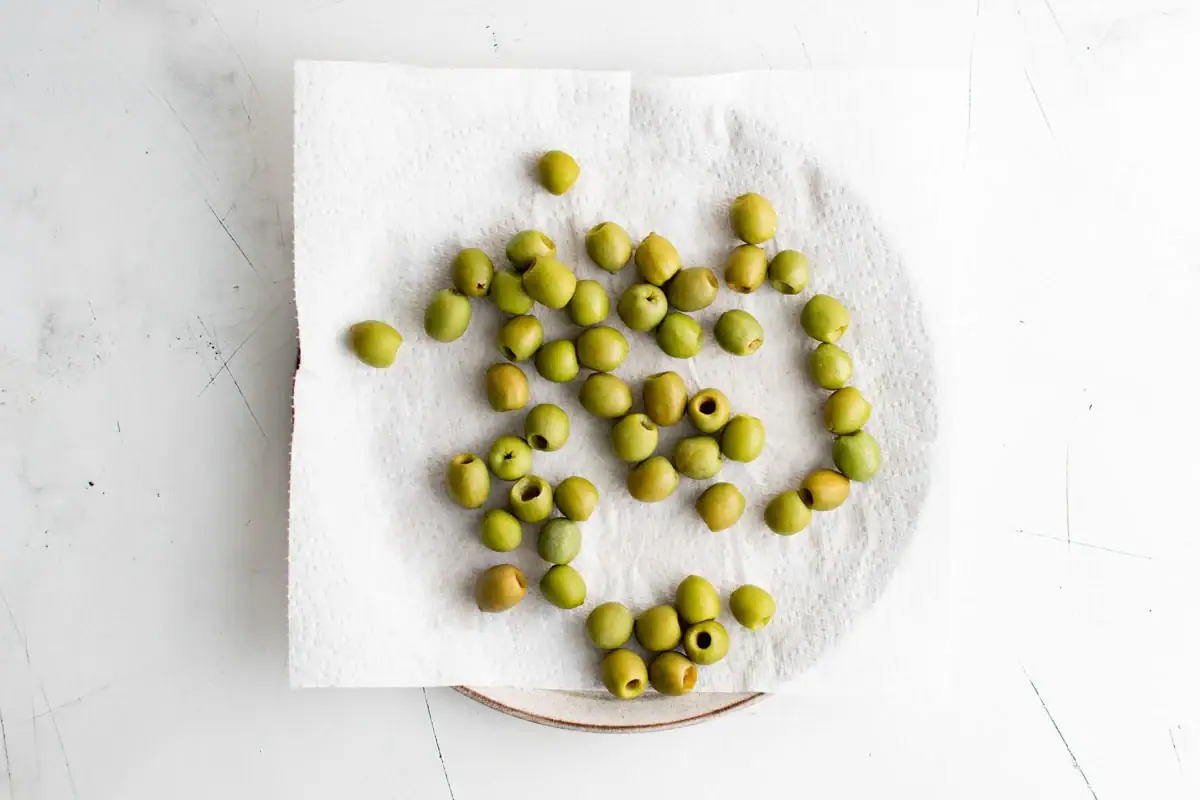Green olives on a paper towel on a plate.