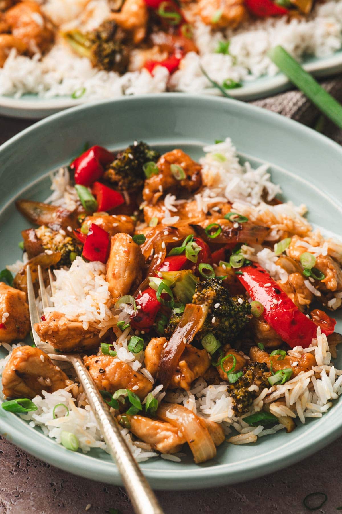 Chicken stir fry served over white rice on a light blue plate with fork