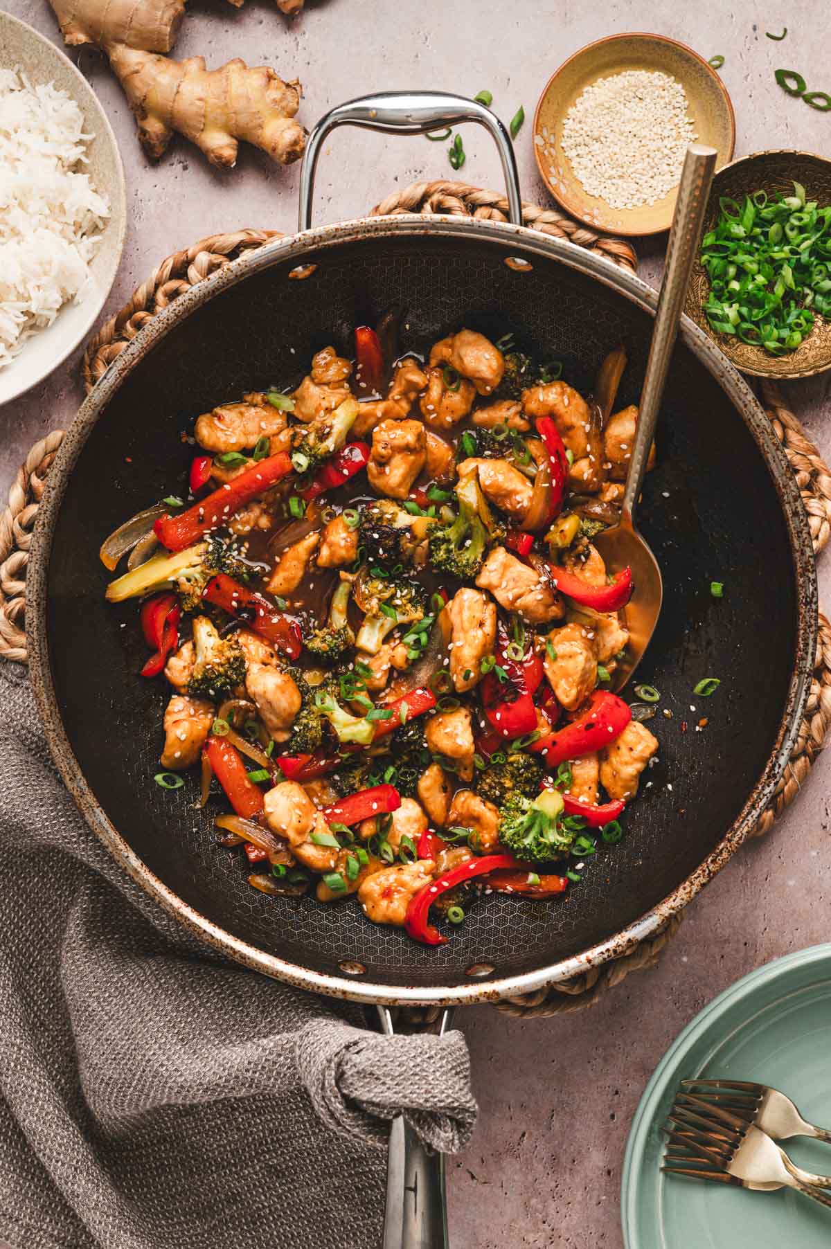 Chicken stir fry in a wok with serving spoon and sesame seeds on top
