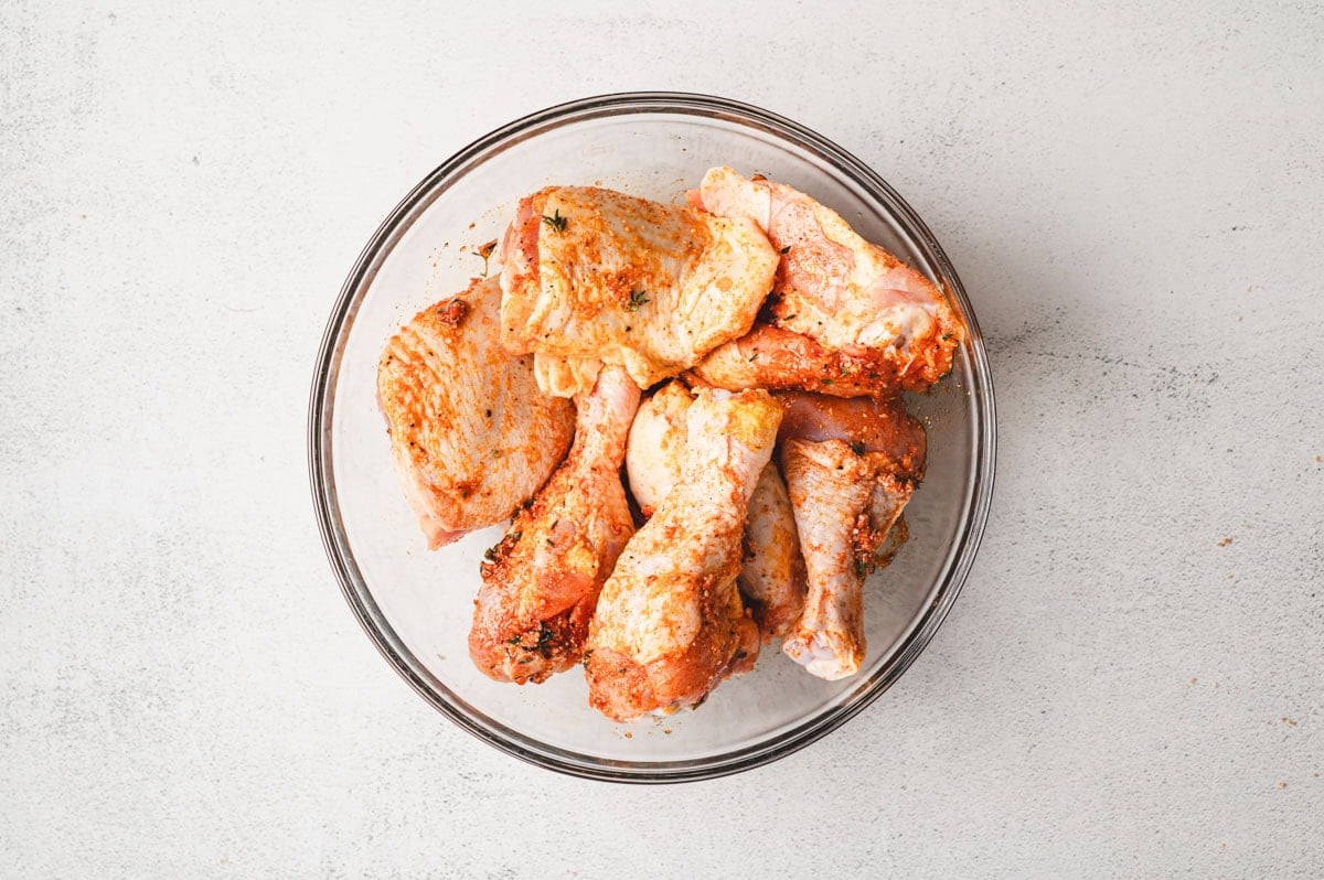 Raw chicken in a glass dish with seasoning on top.