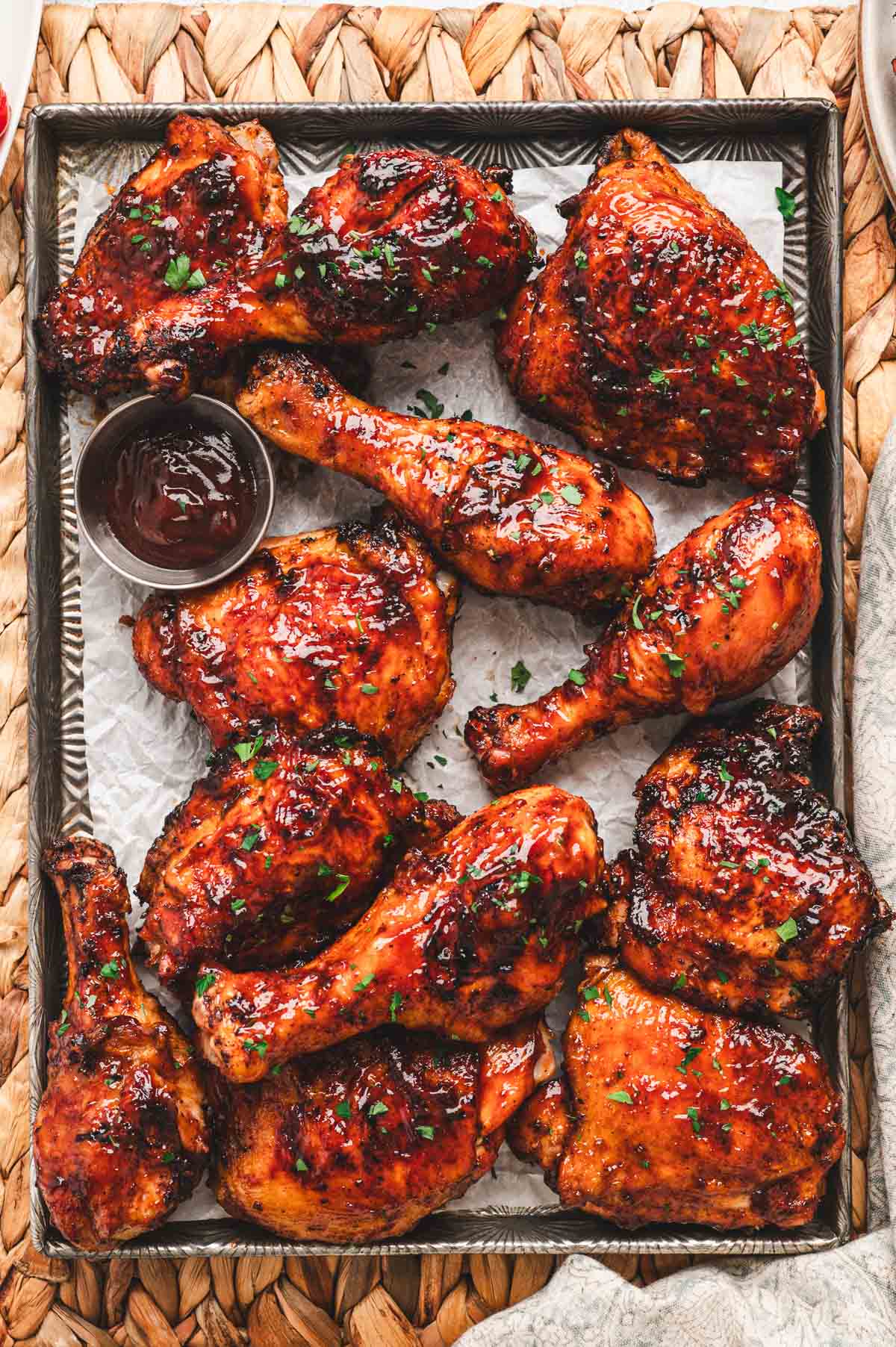 Pieces of grilled bone-in, skin-on chicken slathered with BBQ sauce on a sheet pan.