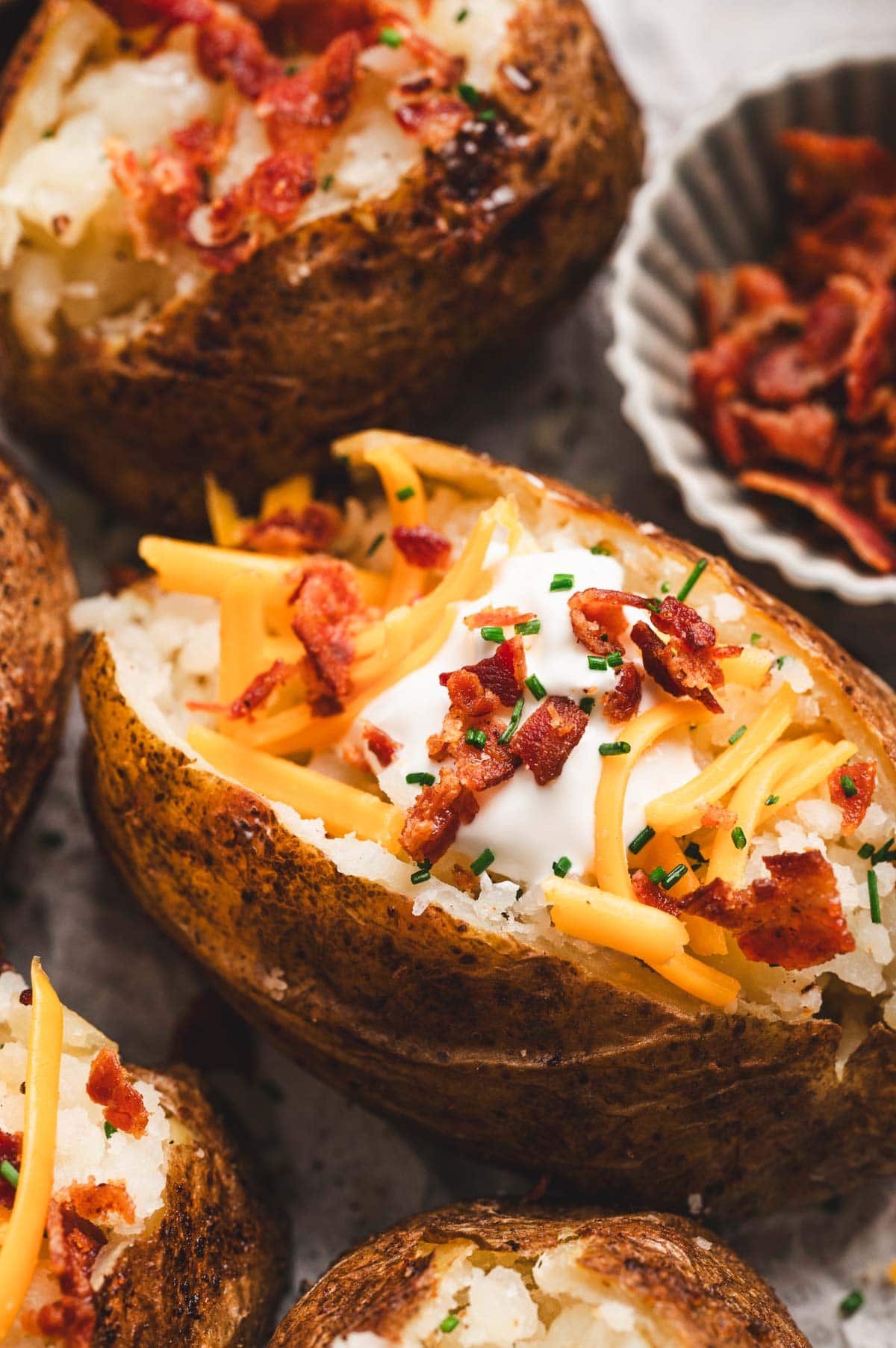 Close up of baked potato topped with shredded cheddar cheese, bacon bits, sour cream, and fresh chopped chives.