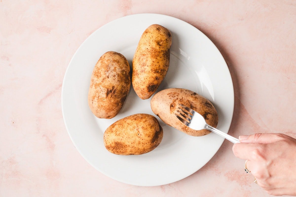 Potatoes on a white plate being poked with a fork.