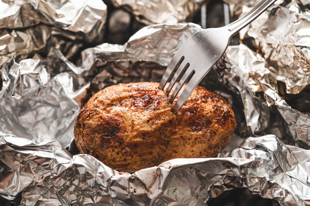 Foil wrapped potato being poked with a fork.