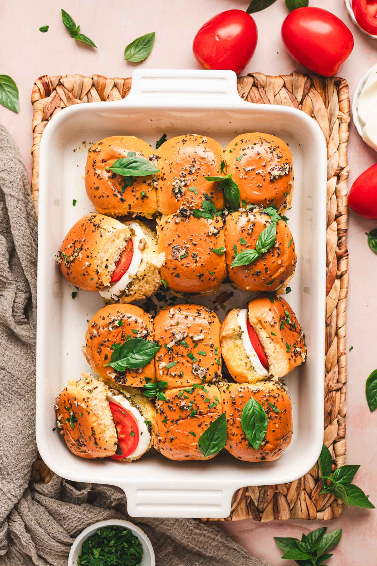 A rectangular dish with hot caprese sliders inside covered in a garlic herb butter with fresh basil leaves on top.