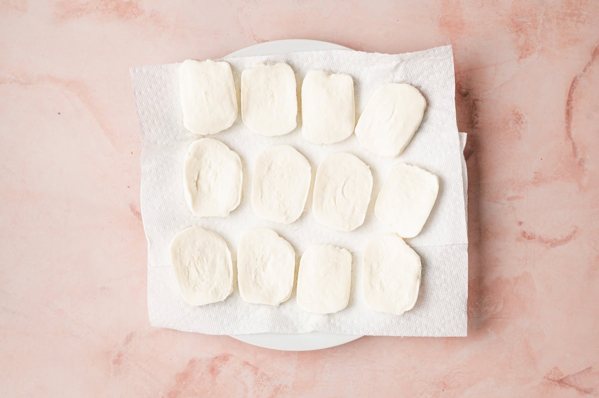 Fresh slices of mozzarella on a paper towel being blotted to remove excess moisture.