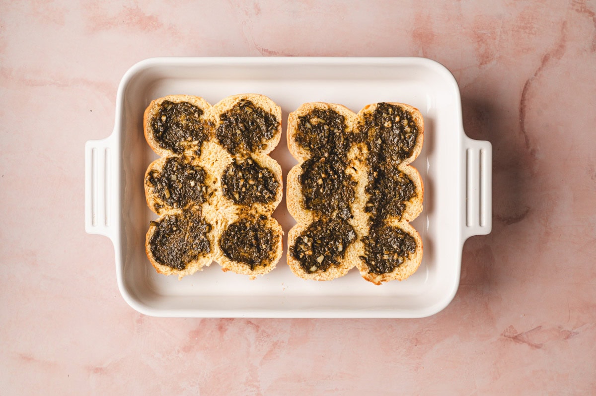 Pesto, balsamic, and seasoning mixture being spread over the toasted buns.