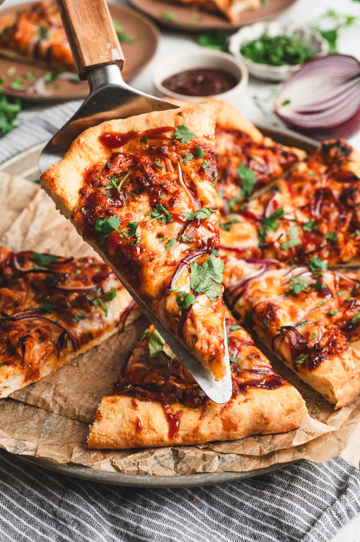A slice of pizza on a pizza spatula being held up above the finished, sliced pizza.