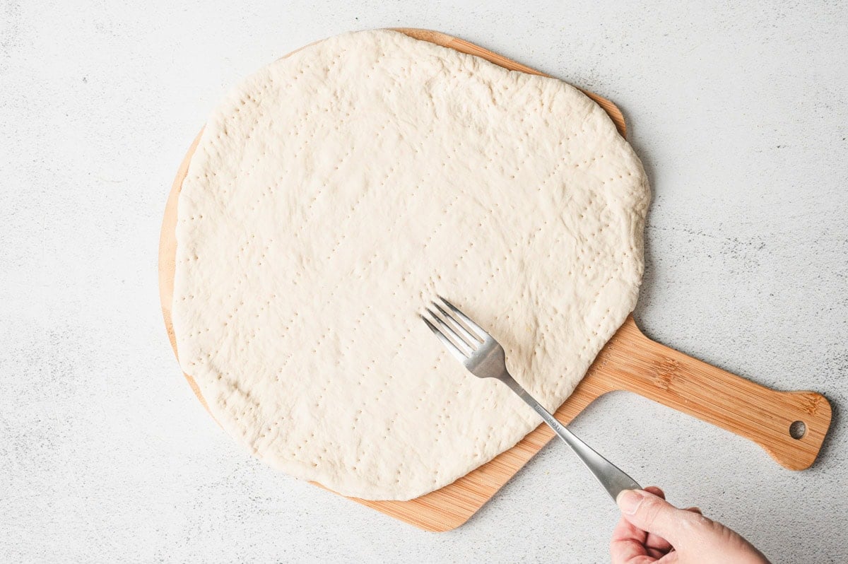 Pizza crust on a wooden pizza peel with holes poked in the dough with a fork.
