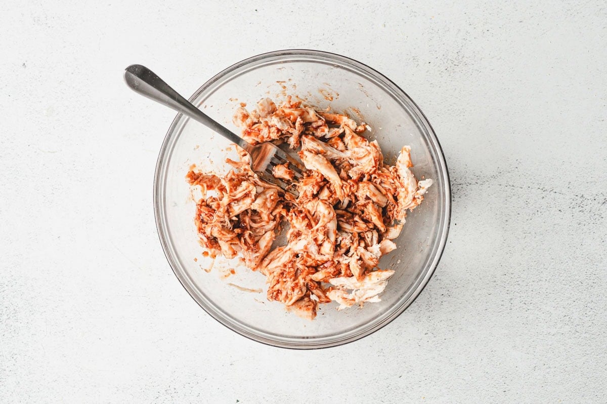 Chicken and BBQ sauce mixed in a glass bowl.