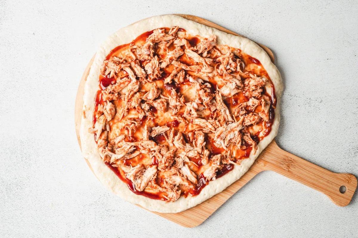 Pizza crust, uncooked, with BBQ sauce and chicken on top.