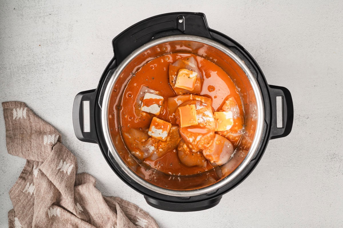 Instant pot with buffalo sauce, chicken and butter inside.