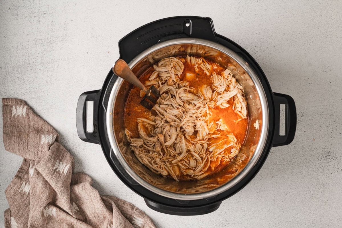 Instant pot with cooked shredded chicken and buffalo sauce inside.