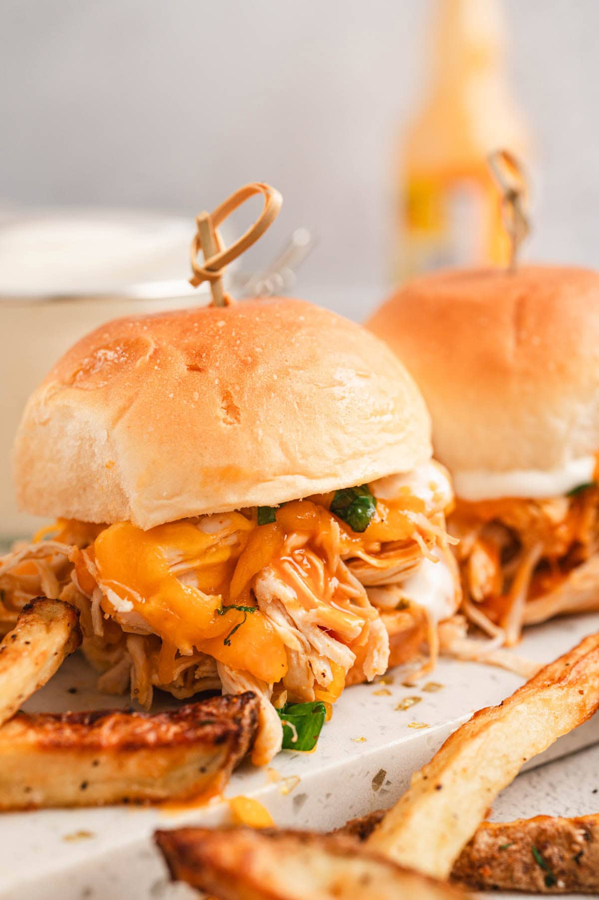 Close up of buffalo chicken sliders next to french fries.