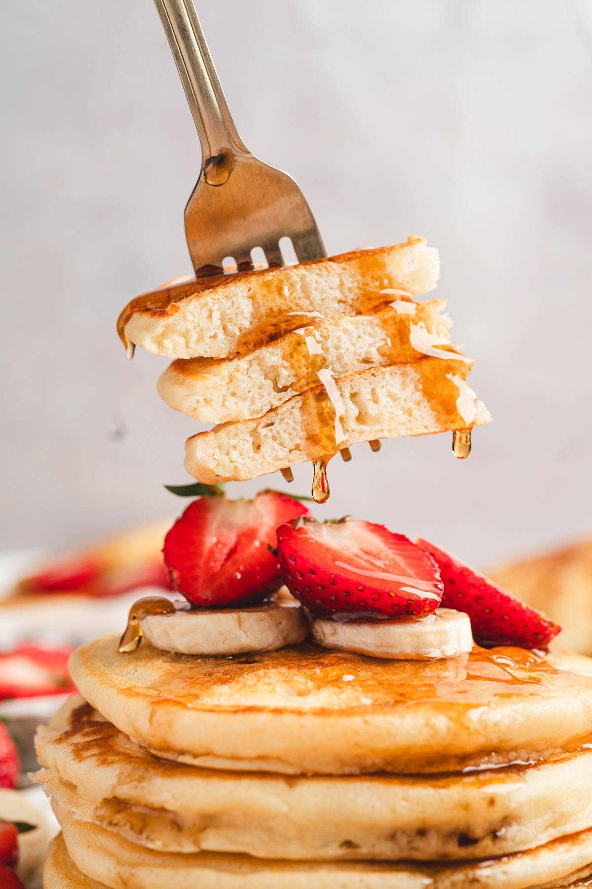 A fork with a bite of three layers of pancakes with maple syrup drizzled on them.