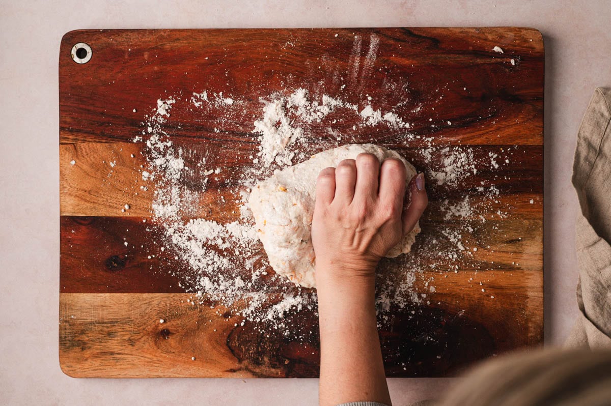 Biscuit dough being kneaded on a wooden board with flour.