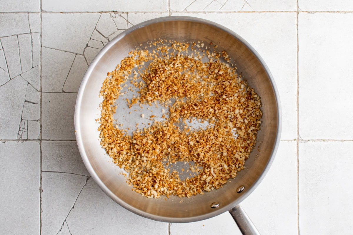 Breadcrumbs being toasted in a stainless steel skillet.