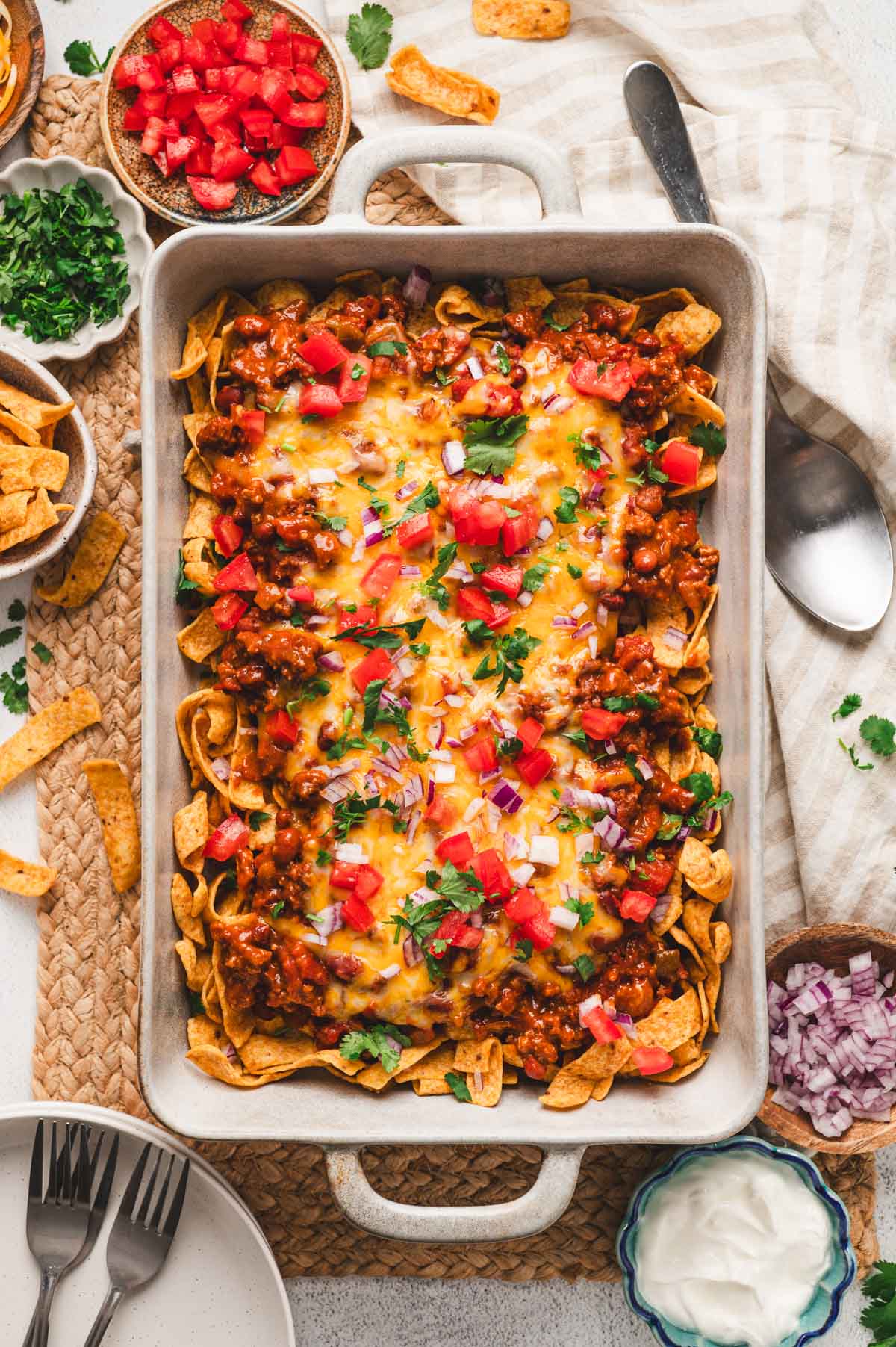 Frito pie in a casserole dish. Layers of fritos, chili, cheese, tomatoes, onions, and cilantro.