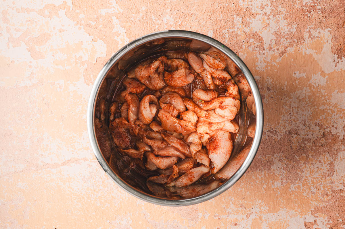 Cut up pieces of raw chicken tossed with spices in a stainless steel pot.