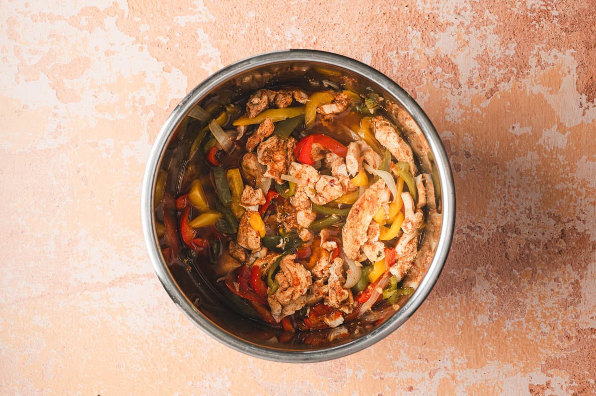 Cooked fajita seasoned chicken, peppers, and onions in a stainless steel Instant Pot.