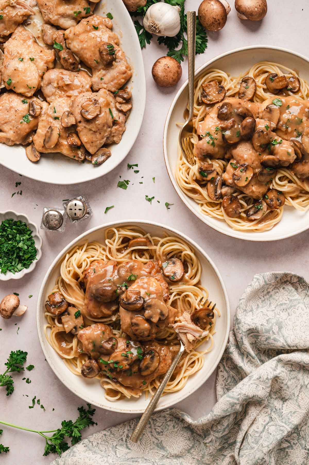 Chicken marsala served over spaghetti on white plates with chopped parsley garnish.