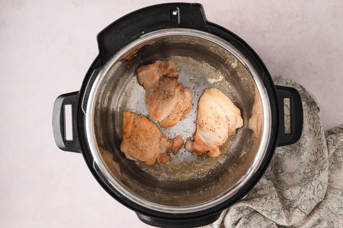 Chicken thighs being browned in an instant pot.