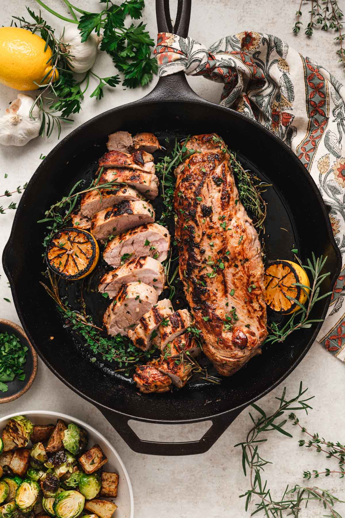 Two pork tenderloins cooked with herbs and lemon in a cast iron skillet.