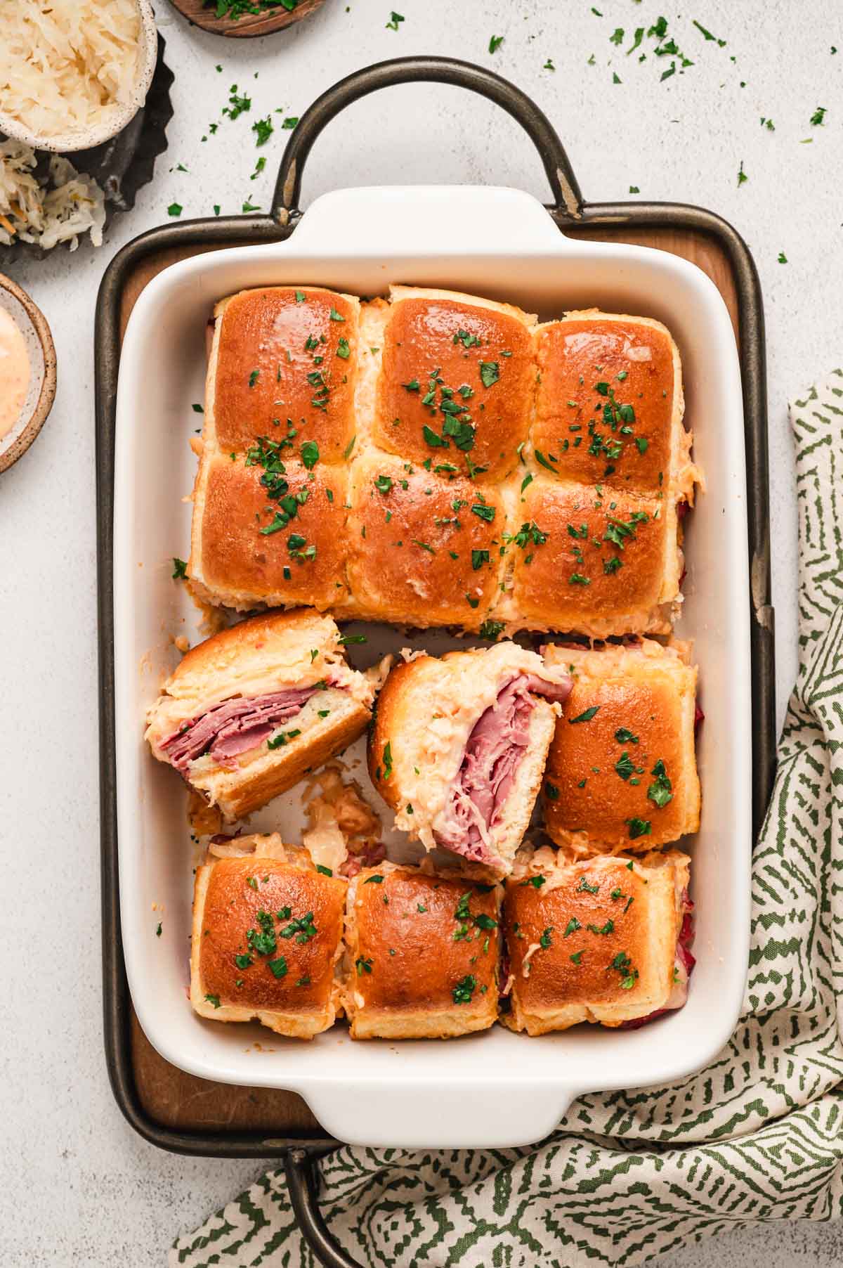 White casserole dish with baked reuben sliders garnished with parsley.