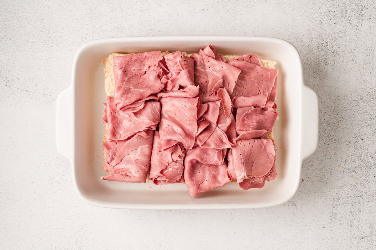 White casserole dish with slider buns topped with corned beef.